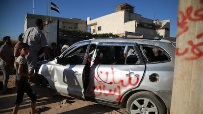 Manifestantes junto a un coche destrozado cerca de una base militar turca de Atarib, en Siria, este lunes.