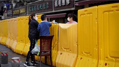 Uma mulher paga a compra de um mercado delimitado por uma barreira levantada durante a quarentena, em Wuhan.
