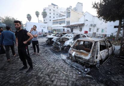 Varias personas observan los restos de los vehículos destruidos en el hospital Al-Ahli de Gaza. 