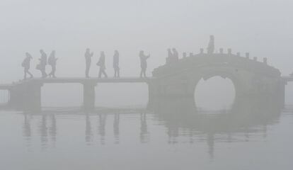 Visitantes caminan sobre un puente del lago del Oeste, en medio de una espesa niebla y humo pesado en Hangzhou (China).