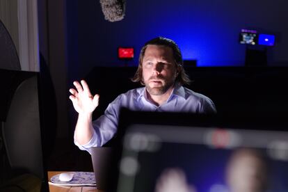 Ken Joyce - Looking up to the left of the camera, hand in the air, sitting at desk, Shadows on right side of face and body