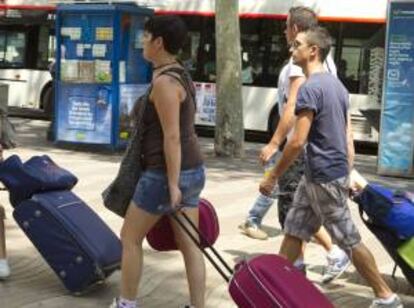 Varios jovenes turistas arrastran sus maletas camino a su hotel en las populares Ramblas de Barcelona en el inicio de las vacaciones estivales de agosto. EFE/Archivo