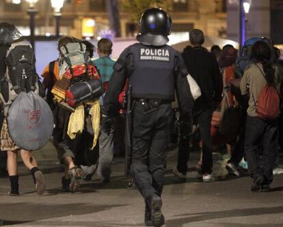 Varios acampados abandonan la plaza de Catalunya bajo la mirada de un 'mosso'.