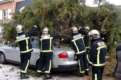 Los bomberos retiran un árbol caído sobre un coche en la localidad madrileña de Collado Mediano.