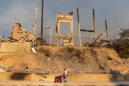 Una mujer que lleva algunas de las pertenencias que ha sacado de su casa pasa bajo los restos de una iglesia quemada tras el  incendio de Pacific Palisades, en Los Ángeles, el 10 de enero de 2025.