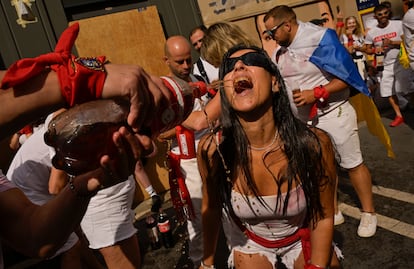 A woman drinks wine out of a traditional "bota" while waiting for the launch of the 'Chupinazo' rocket.