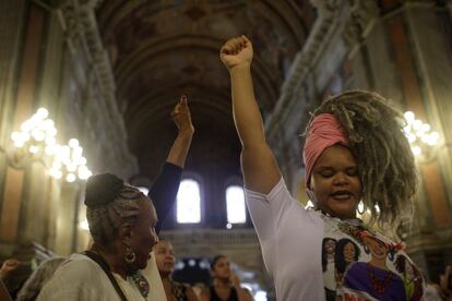 Dos mujeres alzan los brazos durante una misa por el primer aniversario del asesinato de la activista y concejala Marielle Franco, en Río de Janeiro (Brasil).