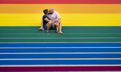 Una pareja se besa sobre una gran bandera gay instalada en Roosevelt Island, Nueva York.