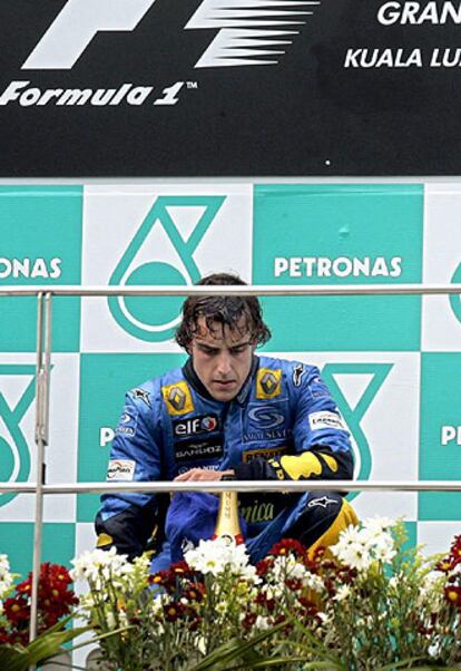 Fernando Alonso, en cuclillas en el podio, busca recuperar la respiración.