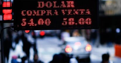 Transeúntes caminando bajo un letrero luminoso que informa el valor de compra y venta del dólar, en Buenos Aires (Argentina).