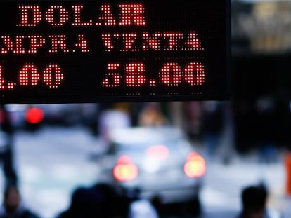 Transe&uacute;ntes caminando bajo un letrero luminoso que informa el valor de compra y venta del d&oacute;lar, en Buenos Aires (Argentina). 