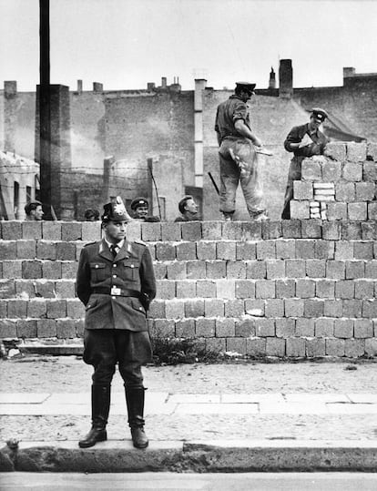 Un policía de Berlín Occidental hace guardia frente la tapia que lo separa de la zona comunista, mientras varios albañiles trabajan en la construcción para hacer más alto el Muro.