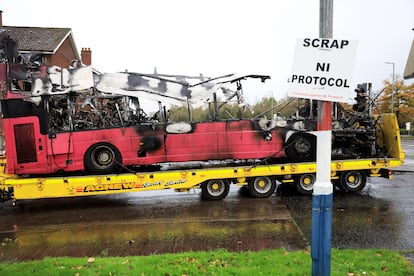 Los restos del autobús incendiado en Belfast, este lunes. Frente al vehículo, un cartel exige la retirada del Protocolo de Irlanda del Norte.