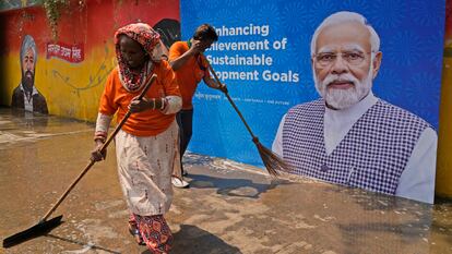 Dos trabajadores limpian la calle delante de un cartel de Modi en Nueva Delhi el jueves.