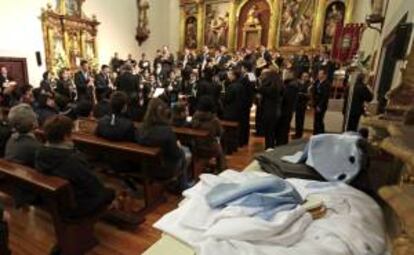 Los trajes de varios cofrades de la Hermandad Penitencial Nuestro Padre Jesús Atado a la Columna reposan junto a un altar en el interior de la iglesia donde actúa la banda de música, tras suspenderse la Procesión General de esta tarde en Valladolid ante el riesgo de lluvia.