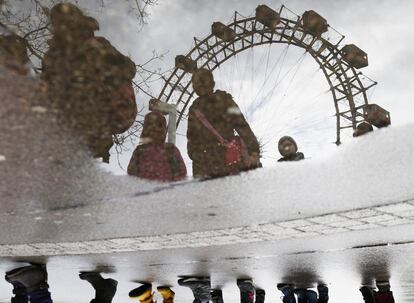 Unos niños reflejados en un charco de las calles de Viena (Austria) en el que también se puede ver el Riesenrad (la noria gigante) de Wurstelprater, el parque de atracciones más antiguo del mundo.