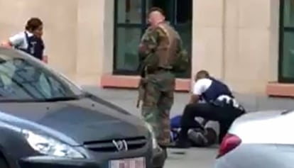 Polic&iacute;as y un soldado rodean a un hombre tendido en el suelo en el lugar donde dos soldados han sido atacados en el centro de Bruselas. 