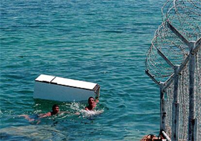 Dos marroquíes pasan un frigorífico a nado al otro lado de la frontera de Tarajasl, en Ceuta.