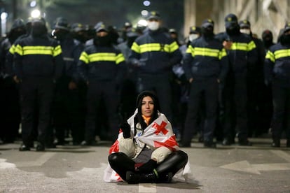 Una mujer cubierta con con la bandera de Georgia sentada frente a la policia, en los alrededores del Parlamento del país caucásico.