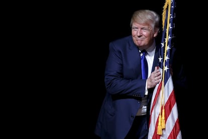 O aspirante republicano à presidência dos Estados Unidos Donald Trump abraça a bandeira de seu país depois de subir ao palco onde celebrou um ato eleitoral em Derry, New Hampshire.