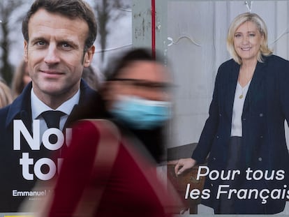 A woman passes by electoral campaign posters of French President and La Republique en Marche (LREM) party candidate for re-election Emmanuel Macron (L) and French far-right party Rassemblement National (RN) presidential candidate Marine Le Pen in Savenay, western France on April 19, 2022. - Emmanuel Macron won 27.85 percent of votes in the first round of France's presidential election, while far-right veteran Marine Le Pen scored 23.15 percent, according to final results from the interior ministry on April 18, 2022. (Photo by Loic VENANCE / AFP)