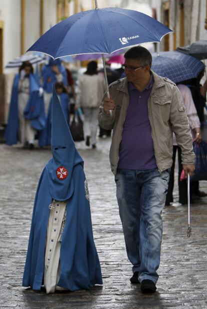 Un joven nazareno de la sevillana Hermandad de San Esteban, resguardado de la lluvia el pasado martes.