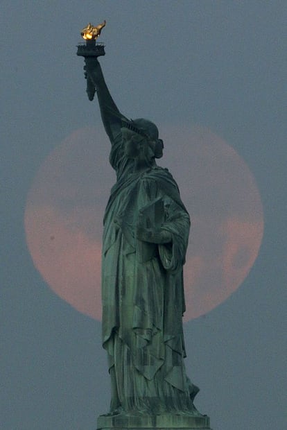 La estatua de la Libertad con una gran luna llena a sus espaldas.