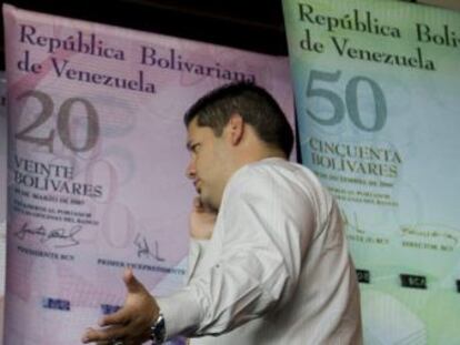 Un hombre habla por tel&eacute;fono mientras camina frente a afiches de billetes venezolanos en la sede del Banco Centra de Venezuala (BCV).