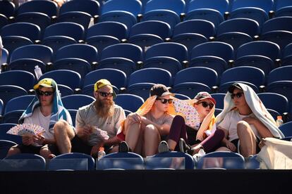 Un grupo de personas se protege del sol mientras asiste al partido de individuales entre la alemana Angelique Kerber y la eslovena Polona Hercog, en el primer día del torneo de tenis Abierto de Australia, en Melbourne.
