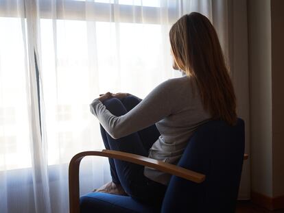 Una mujer sentada en un sillón mira por la ventana en una imagen de archivo.