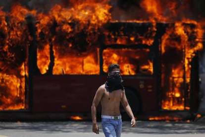 Un manifestante camina cerca de un autobús que fue incendiado por opositores del presidente de Venezuela, Nicolás Maduro.