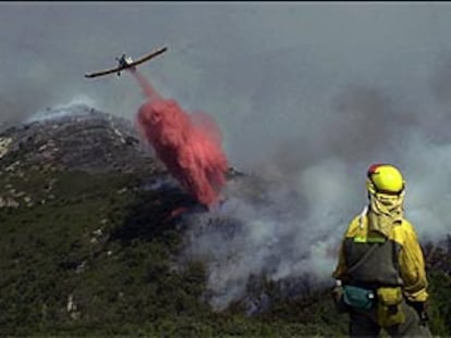Un avión descarga agua sobre el fuego ayer en lo alto del Turmell, en Xert, ante la mirada de un bombero forestal.