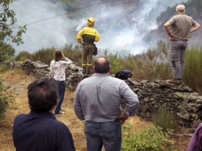 Un brigadista y varios vecinos miran un foco del incendio que asol&oacute; el t&eacute;rmino municipal de Navia de Suarna (Lugo).
