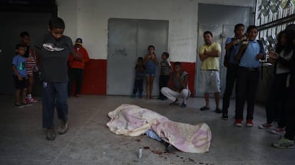 Personas pasan al lado del cuerpo de un manifestante que fue impactado por una bala durante las protestas en Caracas.