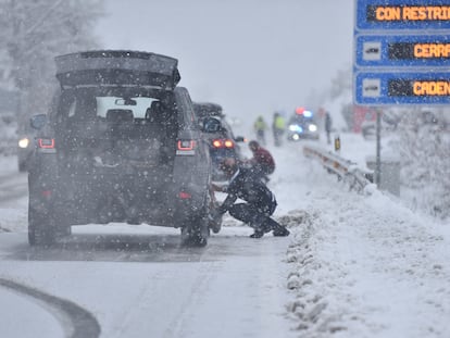 Varias personas ponen cadenas a los coches para poder circular por la carretera nevada, en Huesca este lunes.