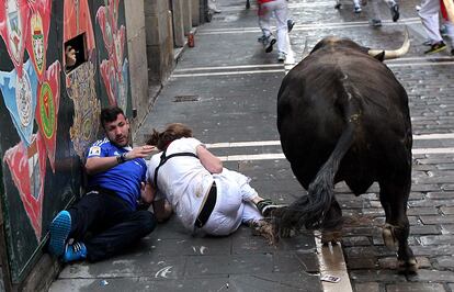 Uno de los toros de Dolores Aguirre pasa junto a dos corredores en la calle Estafeta.