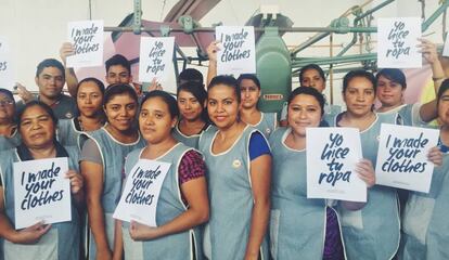 Trabajadoras encargadas de coser la ropa con carteles del Fashion Revolution Day. 