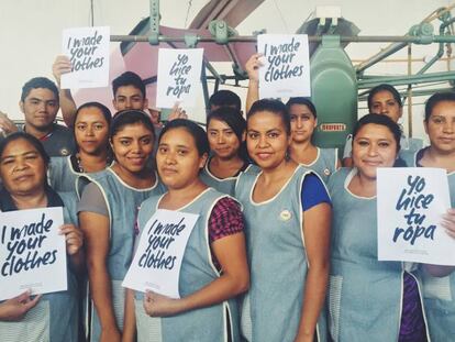 Trabajadoras encargadas de coser la ropa con carteles del Fashion Revolution Day. 