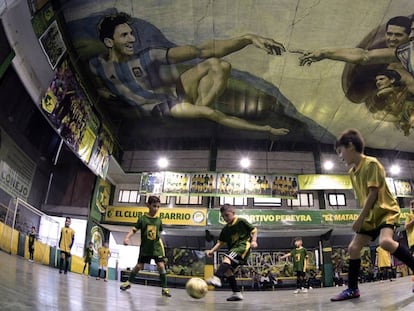 Niños juegan fútbol sala en Sportivo Barracas, un club de barrio de Buenos Aires. En el techo, la versión del artista local Santiago Barbeito de 'La Creación de Adán', con Messi y Maradona, entre otros.