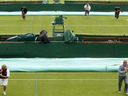 Trabajadores del torneo de Wimbledon extienden lonas sobre el césped de unas pistas del complejo tenístico.