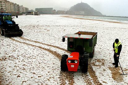 Operarios del servicio de limpieza trabajan en la playa de la Zurriola de San Sebastián, cubierta de nieve.