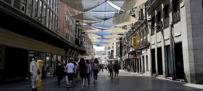 Varias personas pasean por la calle Preciados de Madrid, cubierta con toldos para tapar el sol.