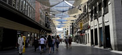 Varias personas pasean por la calle Preciados de Madrid, cubierta con toldos para tapar el sol.