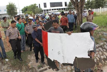 Vecinos de Batam, acompañados por policías, llevan piezas del avión de Qantas que cayeron sobre una zona industrial del pueblo, en Indonesia..