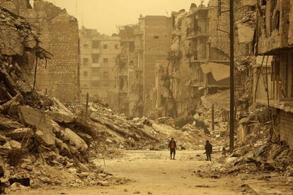 Dos sirios caminan entre los escombros durante una tormenta de arena en el barrio de Kastal al-Harami, en Alepo (Siria).