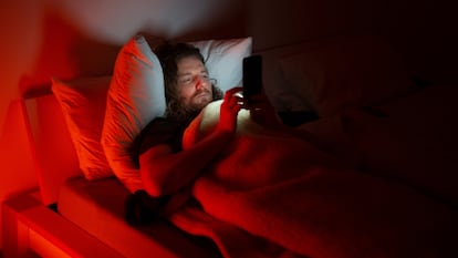 Hombre en la cama con el mvil por la noche y una luz roja como iluminacin.