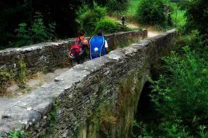 Una pareja de peregrinos atraviesa un puente de piedra en su camino hacia Santiago.
