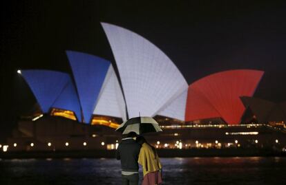 Una parella es cobreix de la pluja a Sydney (Austràlia). Al fons, l'Òpera de Sydney il·luminada amb els colors nacionals de França, en solidaritat amb els atemptats que han costat la vida a 127 persones a París.