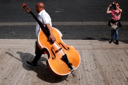 A street musician carries a contrabass as a little girl takes a pictures with a mobile phone on May 5, 2015 in Rome. AFP PHOTO / ALBERTO PIZZOLI