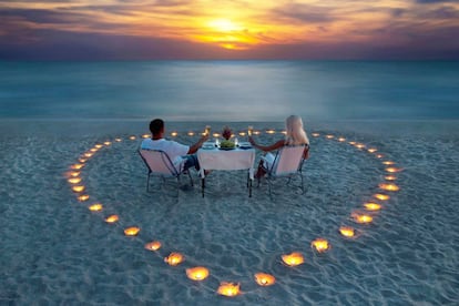 Una pareja cena en una playa a la luz de las velas.